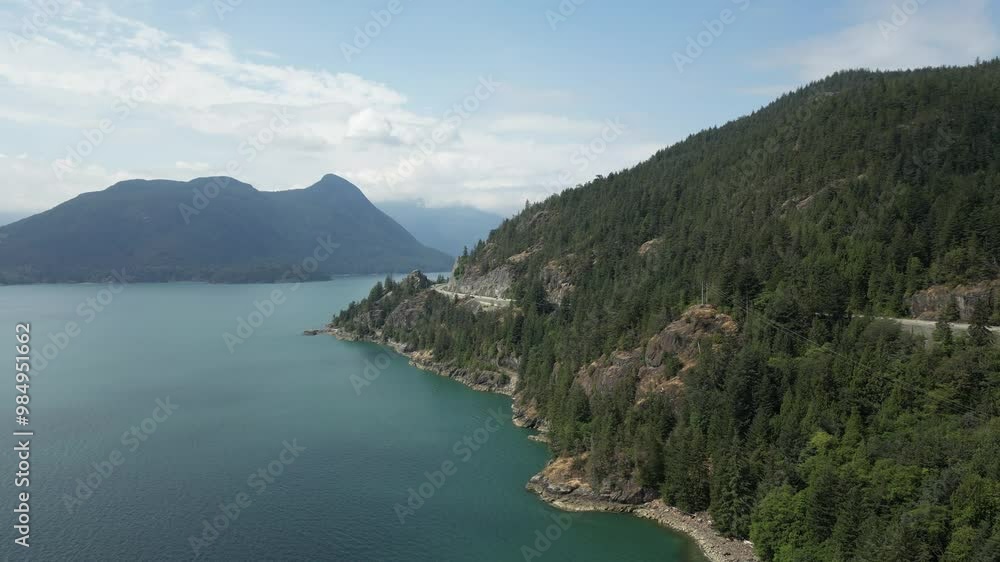 Beautiful aerial view of the Sea to Sky Highway in British Columbia on a sunny day with blue skies, mountains, forest, and turquoise water. British Columbia, Canada. Beautiful aerial view of the Sea to Sky Highway in British Columbia on a sunny day with blue skies, mountains, forest, and turquoise water. British Columbia, Canada.