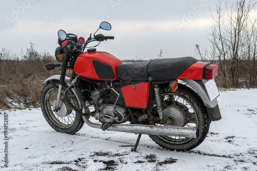 A red Soviet-era Izh motorcycle stands out against a snowy winter landscape, its bold color contrasting with the white surroundings. Riding a motorcycle in winter. photo