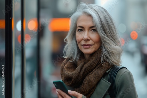 Wallpaper Mural Businesswoman in a coat and scarf holding a smartphone while waiting in a bustling city street during a foggy morning Torontodigital.ca