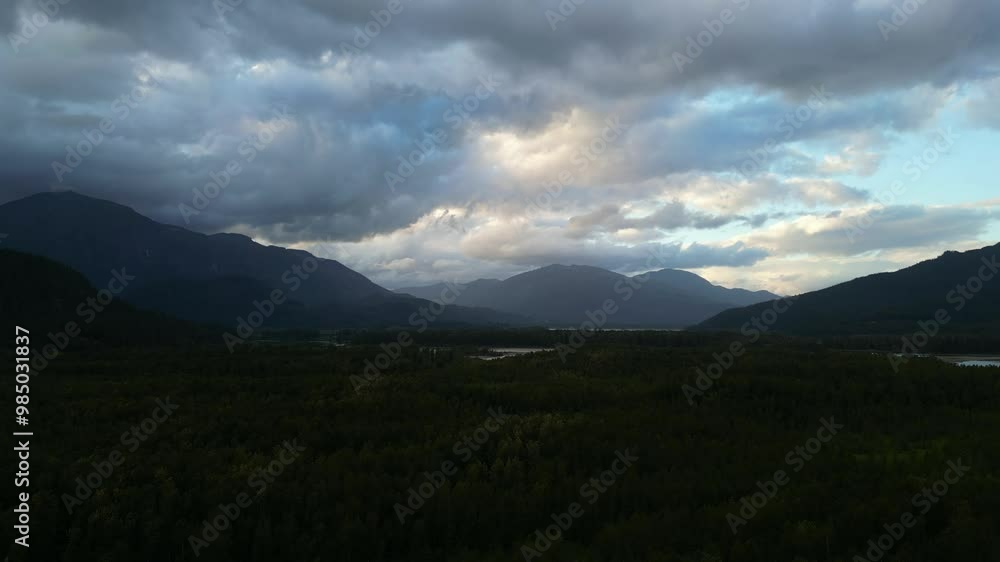 Aerial view of forest and river leading to mountains. Beautiful landscape with dramatic clouds in the sky. British Columbia, Canada. Aerial view of forest and river leading to mountains. Beautiful landscape with dramatic clouds in the sky. British Columbia, Canada.