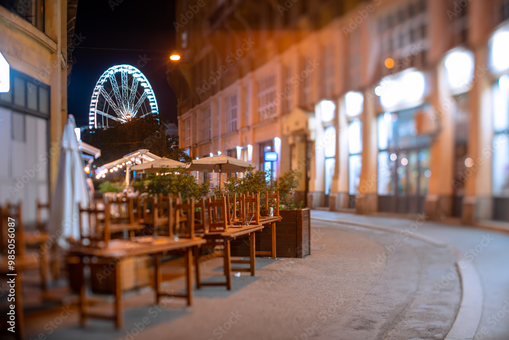 Naklejka premium Budapest, Hungary - August 10, 2024: View to the ferris wheel from Anker koz street at night. Focus tilted to the ferris wheel.