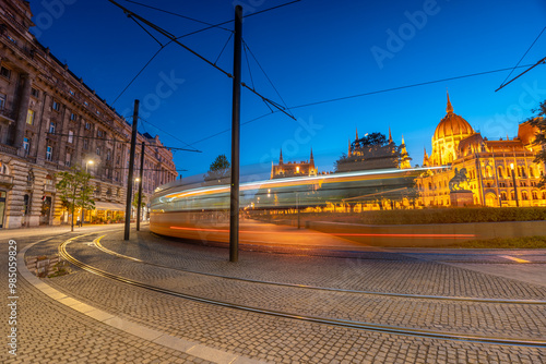 Budapest, Hungary: July 08, 2024: Tram motion blur line. Lajos Square at twilight. Parliament on the background. Long exposure shot. photo