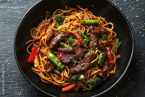 Stir fry noodles with vegetables and beef in black bowl. Slate background. Close up. Top view.
