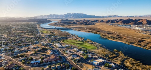 Aerial view of Bullhead City with the Colorado River flowing in the background. Houses and buildings are visible in the city, surrounded by trees and a scenic waterfront.