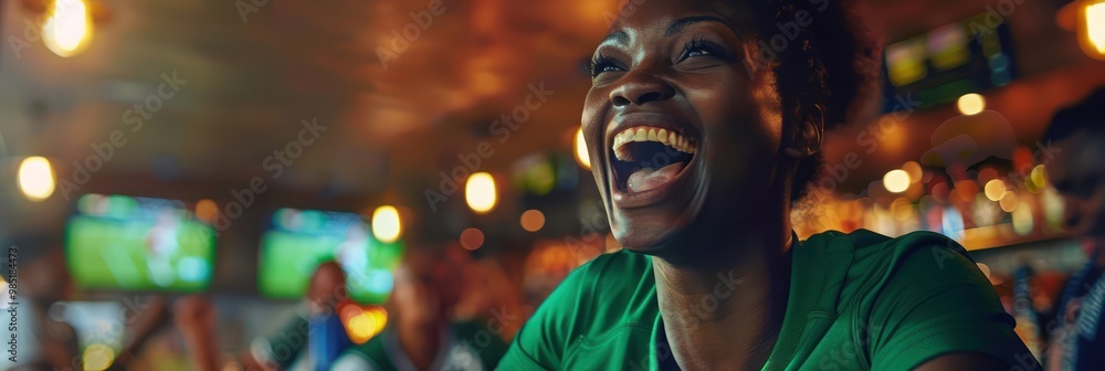 Woman in green shirt laughs and smiles while engaging in conversation at a sports bar, surrounded by people enjoying drinks and food near a TV screen displaying a game. Woman in green shirt laughs and smiles while engaging in conversation at a sports bar, surrounded by people enjoying drinks and food near a TV screen displaying a game.