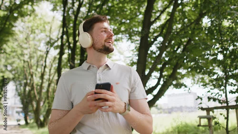 Athletic fitness sport runner guy sportsman walking and using smartphone listening music with wireless headphones. Workout cardio in morning city park. Young man jogger enjoying healthy lifestyle. Athletic fitness sport runner guy sportsman walking and using smartphone listening music with wireless headphones. Workout cardio in morning city park. Young man jogger enjoying healthy lifestyle.