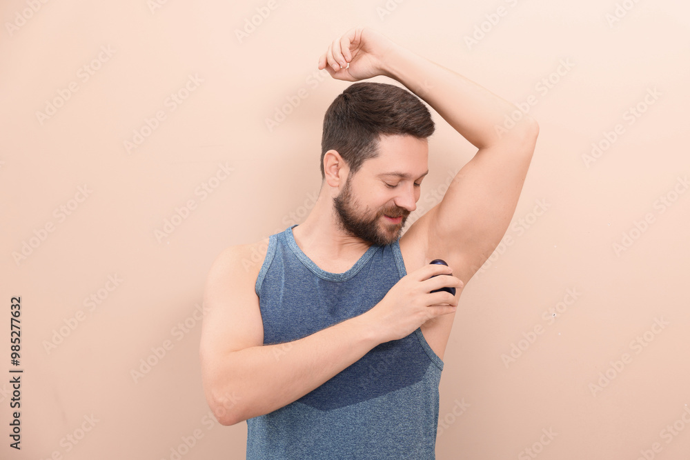 Man applying roll-on deodorant on beige background Man applying roll-on deodorant on beige background