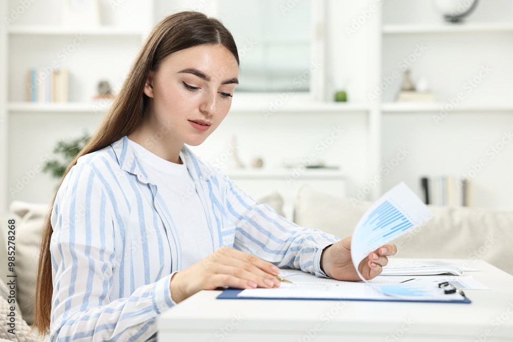 Budget planning. Beautiful young woman with papers at white table indoors Budget planning. Beautiful young woman with papers at white table indoors