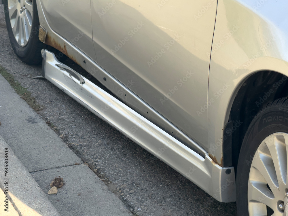 A damaged side skirt on a silver sedan. The skirt is partially ripped off and has visible rust.