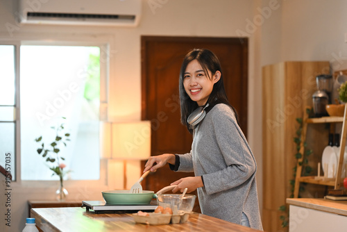 Portrait of cheerful young woman holds a frying pan cooking in modern kitchen