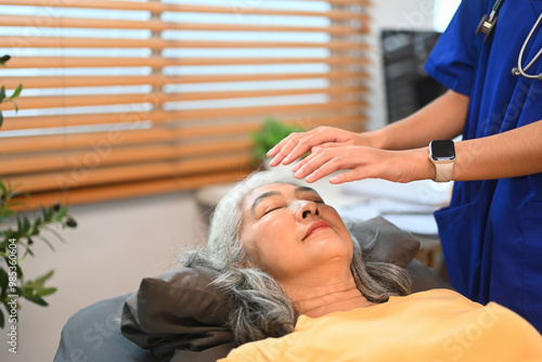 Female practitioner giving Reiki healing treatment to senior patient. Alternative medicine concept photo