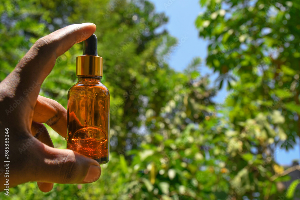 Hand holding a bottle of essential oil in a pipette, natural herb, obtaining oil extracts for medical purposes. dropper bottle in hand and nature background close up. homeopathy, aromatherapy concept Hand holding a bottle of essential oil in a pipette, natural herb, obtaining oil extracts for medical purposes. dropper bottle in hand and nature background close up. homeopathy, aromatherapy concept