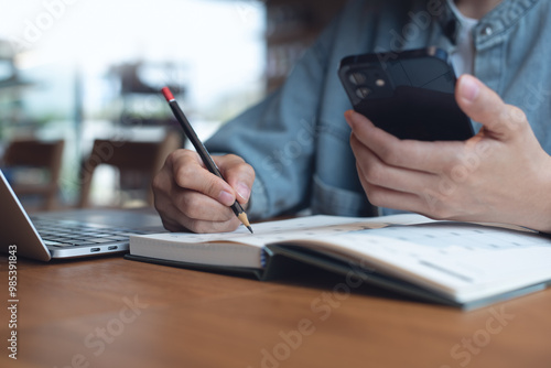 Event planner timetable agenda plan on year 2025 schedule event. Business woman checking planner on mobile phone, taking note on calendar desk on office table. Calendar event plan, work planning photo