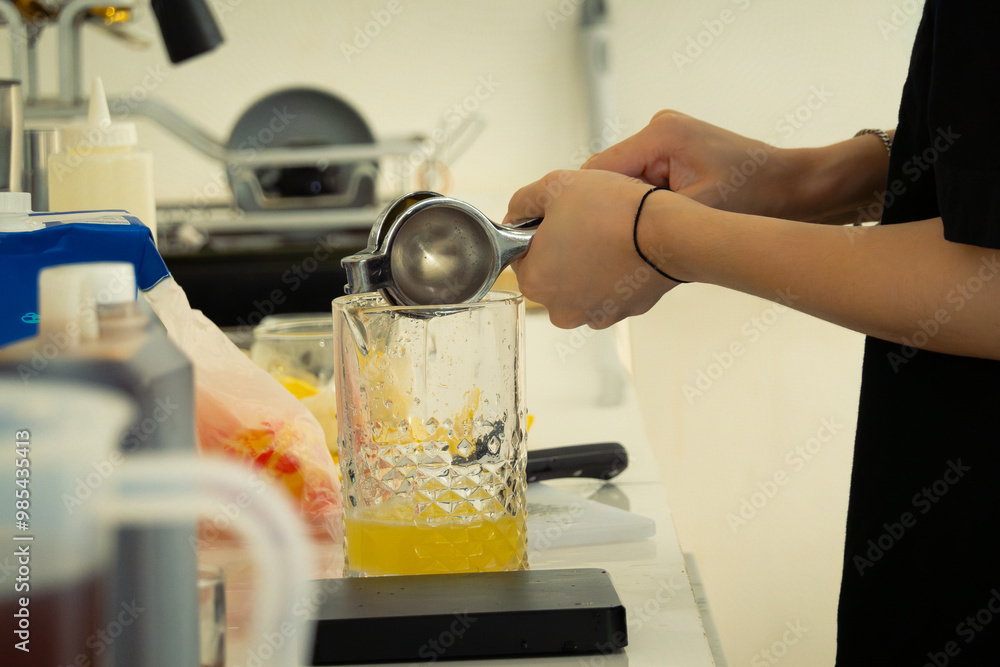 Women barista extracting lemon juice to glass using a lemon squeezer, in a cafe environment. Faceless portrait