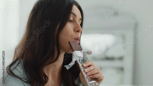 Seizing stress. Close up portrait of young depressed woman eating chocolate, biting bar at home, slow motion photo