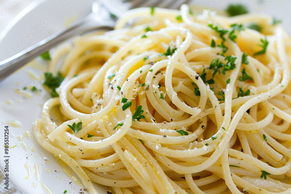 Close-up of a plate of spaghetti tossed with olive oil and thinly sliced garlic. The pasta glistens with oil, garnished with parsley and cracked black pepper. Set on a simple white plate Close-up of a plate of spaghetti tossed with olive oil and thinly sliced garlic. The pasta glistens with oil, garnished with parsley and cracked black pepper. Set on a simple white plate