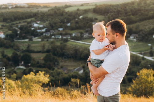 Father Holding Toddler in Scenic Countryside Overlooking a Beautiful Valleyscape at Sunset photo