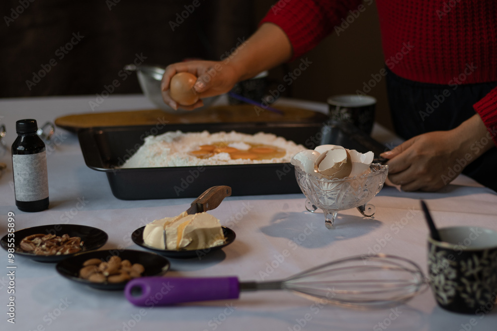 Unrecognizable brown skin woman cracking an egg and mixing it with flour, butter, nuts, vanilla and kitchen utensils ready to prepare the dough. Unrecognizable brown skin woman cracking an egg and mixing it with flour, butter, nuts, vanilla and kitchen utensils ready to prepare the dough.