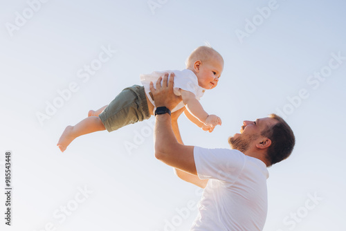 Father Joyfully Lifting Baby in the Air Against Clear Blue Sky photo