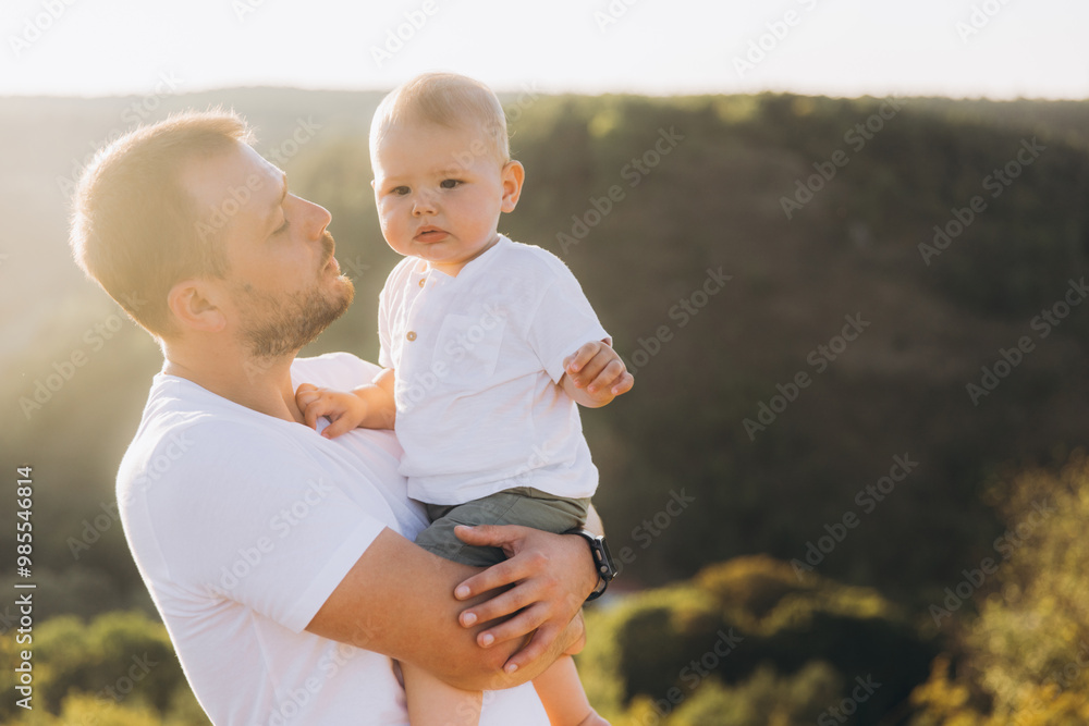 Fototapeta premium Father Holding Baby Outdoors in Nature During Sunset, Expressing Bond and Affection
