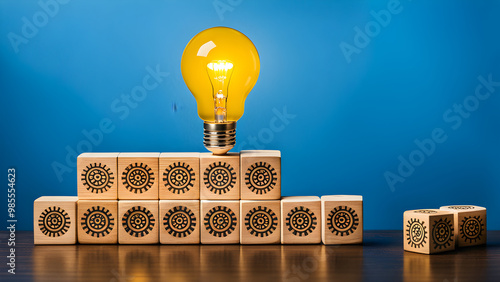 A creative concept of teamwork and innovation represented through wooden blocks. The lower blocks feature heads with gears inside, symbolizing thinking or planning. A top block with a glowing lightbul photo