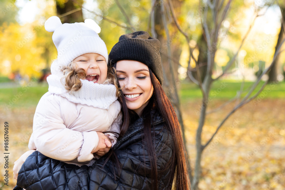 Mother and young little girl with blonde hair are playing in an autumn park on a yellow and orange leaf background Mother and young little girl with blonde hair are playing in an autumn park on a yellow and orange leaf background