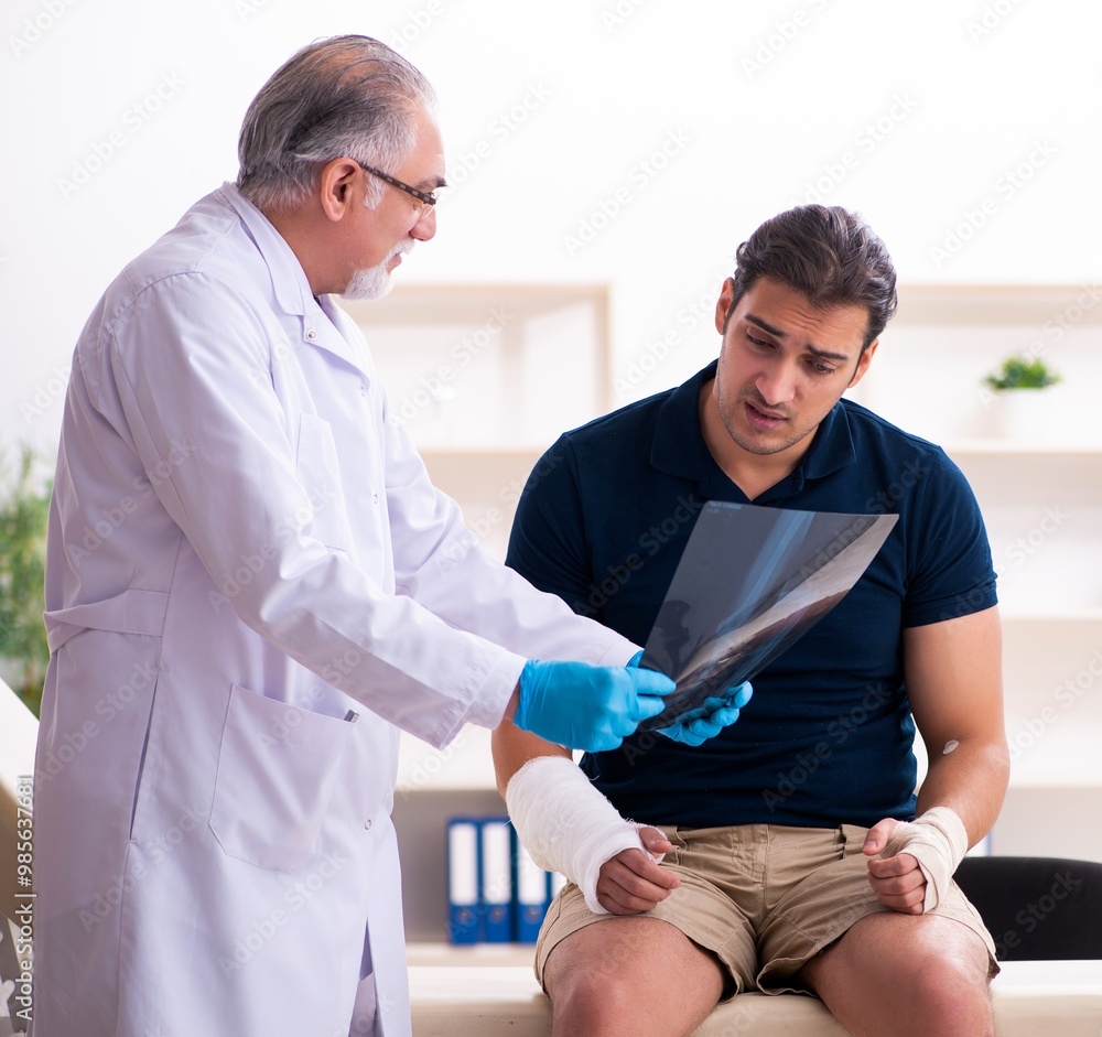 Obraz premium Young injured man visiting old doctor traumatologist