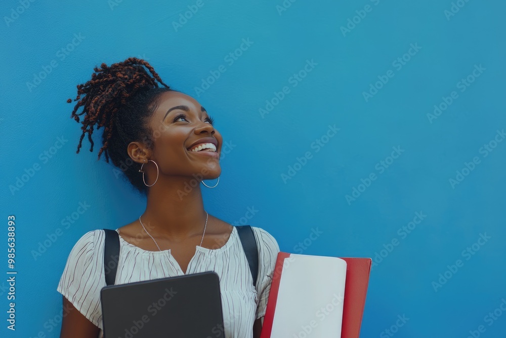 Obraz premium Beautiful African american woman holding files laughing and looking up on a blue wall