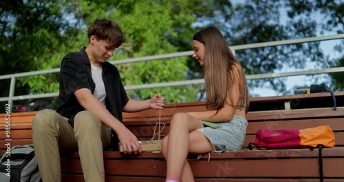 Happy girl schoolgirl communicates with her friend from classmate who opens a box of pizza while relaxing in the park in summer photo