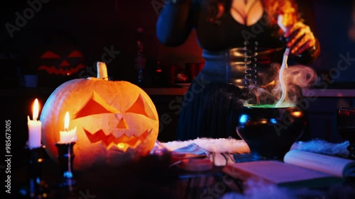 Carving a head from a pumpkin and a candle on the table. The witch makes a potion in a Halloween pot and throws something into it. Mystical Halloween celebration concept. photo