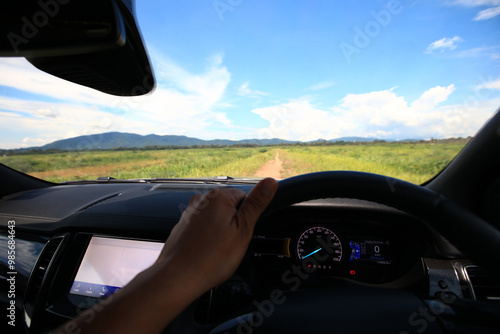 A car driving through a scenic countryside road with mountains in the background and a clear blue sky