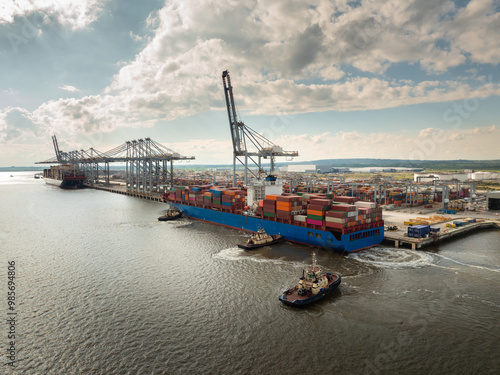 Tug boats push and pull a huge container ship into port for unloading