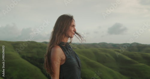 Female enjoy green hills landscape at sunset. Long hair brunette girl looking on beautiful nature scene, hair blowing in wind. Freedom, happiness lifestyle. Travel, tourism, holiday. Slow 4k photo