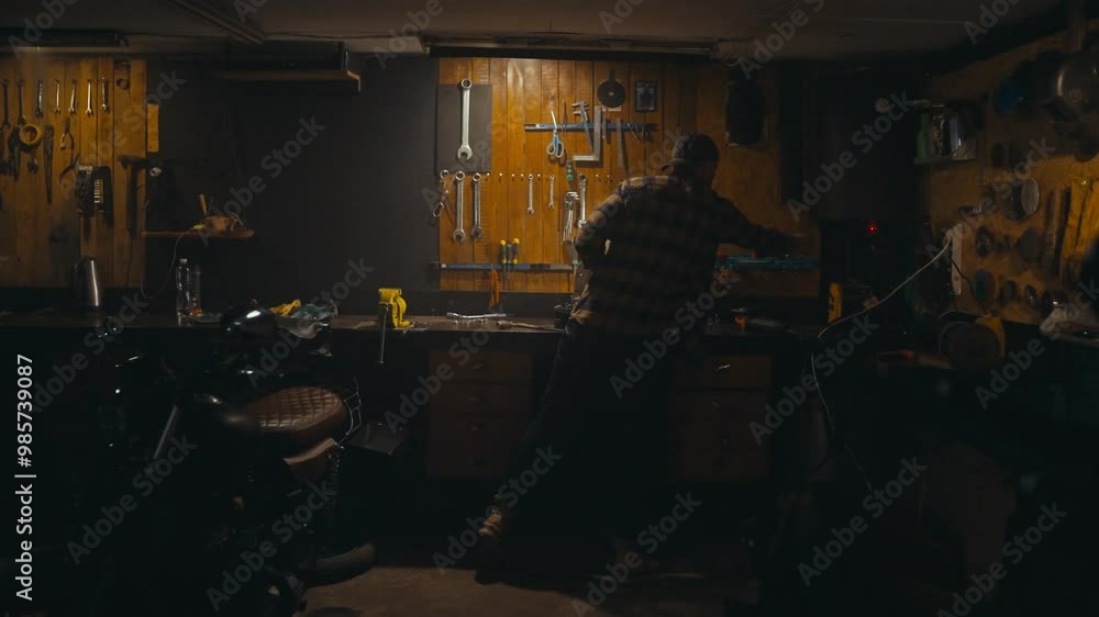 Rear view of a confident guy mechanic in a plaid shirt and yellow gloves working on a workbench among many tools in his cozy studio workshop Rear view of a confident guy mechanic in a plaid shirt and yellow gloves working on a workbench among many tools in his cozy studio workshop