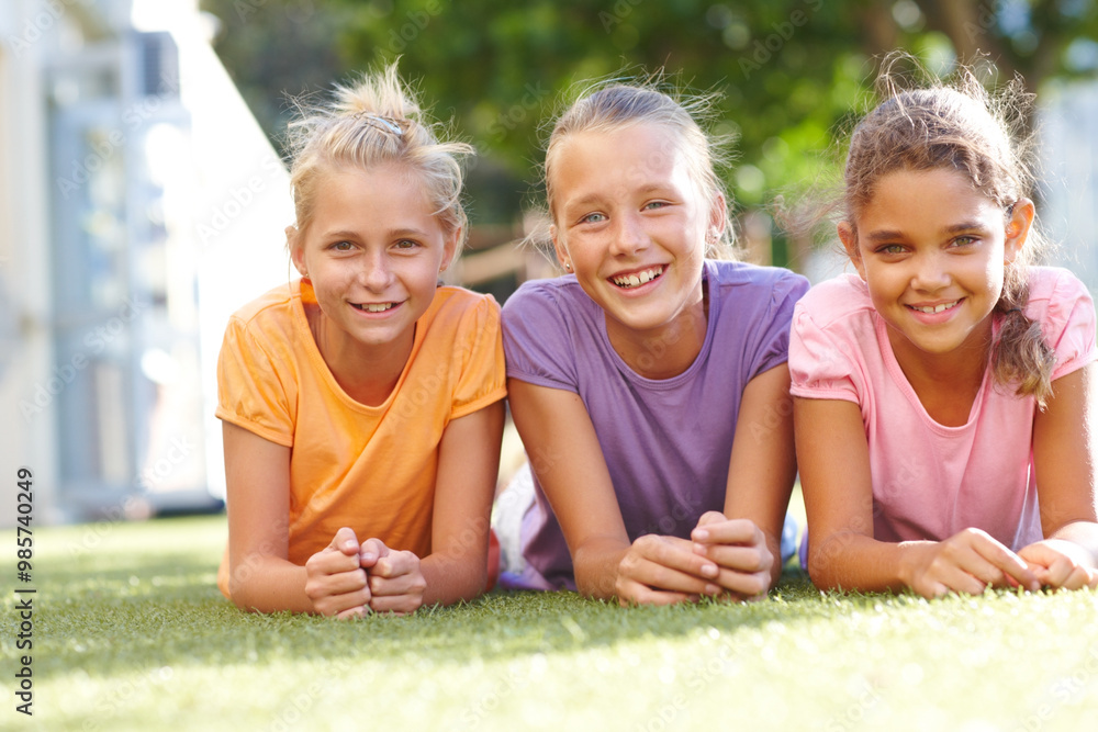 Fototapeta premium Outdoor, friends and children in portrait for lying, connection and bonding together with happiness. Grass, relax and girls with laughing for childhood games, smile and reunion for school holiday