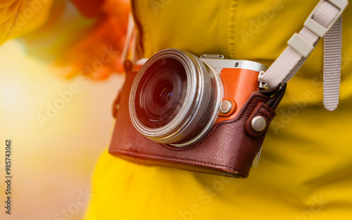 Close-up of a vintage-style camera in a leather case, worn over the shoulder of a person dressed in a yellow jacket. The warm sunlight creates a nostalgic and inviting atmosphere, perfect for promotin photo