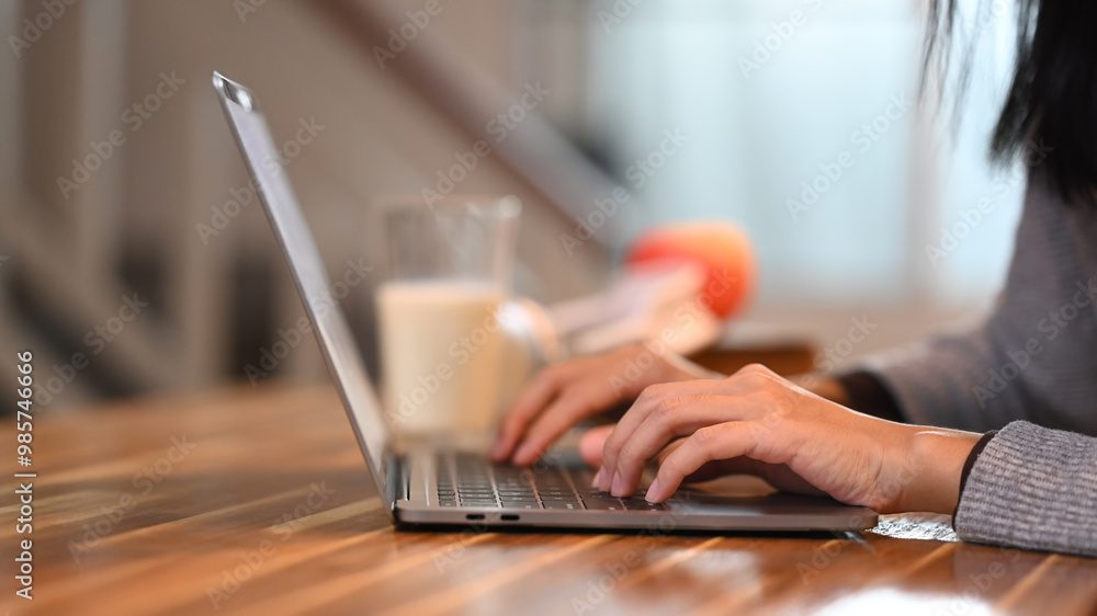 Smiling young asian woman sitting at kitchen table and using her laptop Smiling young asian woman sitting at kitchen table and using her laptop