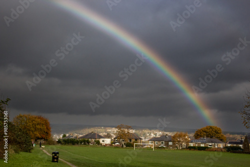 A rainbow's spectrum of colours stands out against a stormy sky over a football field and nearby houses in Cottingley Yorkshire raising thoughts of a pot of gold at its elusive end