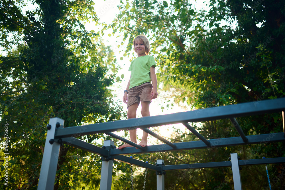 A young child enjoys climbing on a playground structure surrounded by lush greenery on a sunny day A young child enjoys climbing on a playground structure surrounded by lush greenery on a sunny day