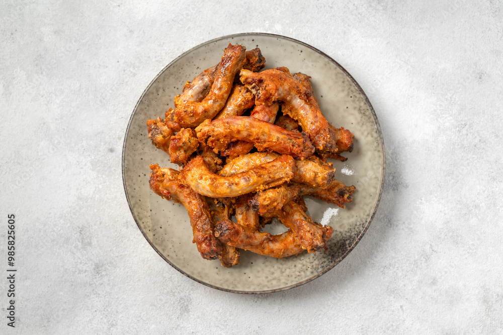 Baked chicken necks in a ceramic plate on a light culinary background top view