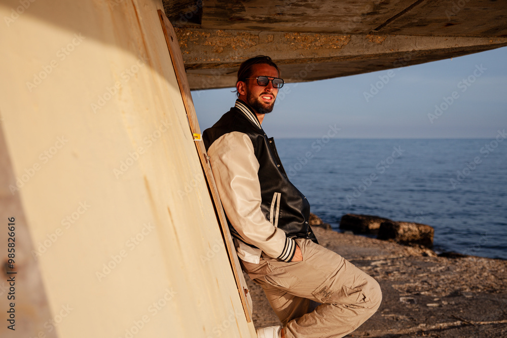 portrait of a handsome and sporty young guy dressed in casual clothes in a seaside location. The model is posing with a smiling expression while standing on a beach at sunset portrait of a handsome and sporty young guy dressed in casual clothes in a seaside location. The model is posing with a smiling expression while standing on a beach at sunset