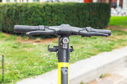 Handlebars of modern electric scooter parked outdoors, close-up view with green park background, urban transport concept