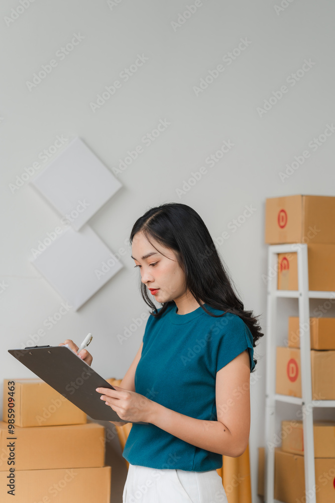 Organized Efficiency: Young Asian entrepreneur meticulously manages orders in her bustling home office, embodying the spirit of e-commerce and small business success. Organized Efficiency: Young Asian entrepreneur meticulously manages orders in her bustling home office, embodying the spirit of e-commerce and small business success.