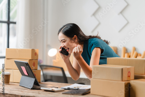 Businesswoman Celebrating Success: A dynamic image of a young entrepreneur, radiating joy and excitement as she celebrates a successful business deal on the phone, surrounded by stacked boxes, symboli