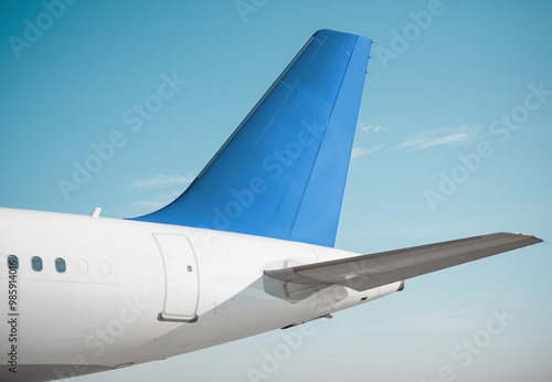 Modern aircraft's tail assembly on a sunny day. Empennage of white airplane with blue vertical stabilizer, clear sky in the background.  photo