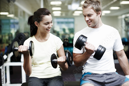 Couple, smile and exercise with weights in gym for bodybuilding, fitness and training together. Man, woman and happy with equipment in health club for strength workout, support or teamwork in morning