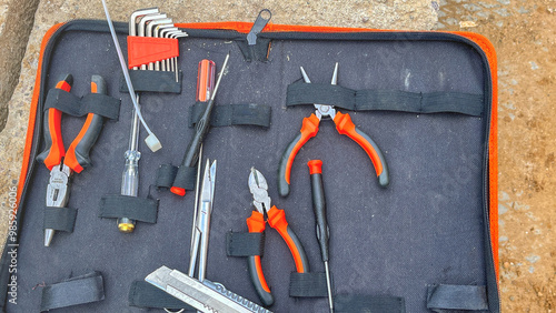 A tool kit is displayed in a black case with a red strap. The tools include a pair of pliers, a pair of scissors, a pair of wire cutters, and a pair of needle nose pliers photo