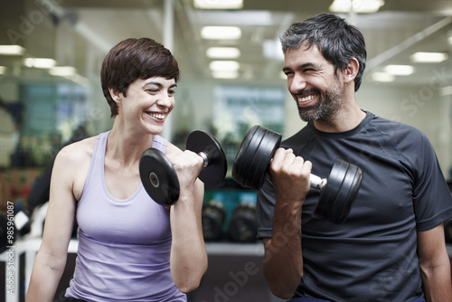 Happy, couple and exercise with weights in gym for bodybuilding, fitness and workout together. Man, woman and smile with equipment in health club for strength training, support or teamwork in morning