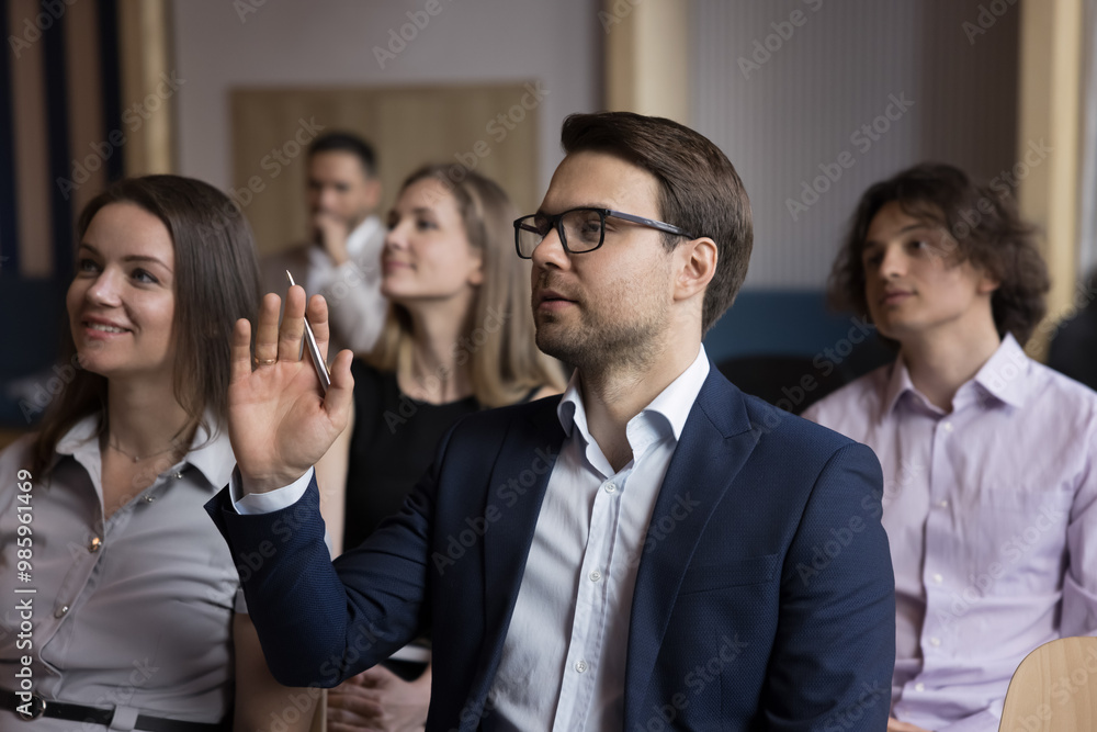 Confident businessman asking question to speaker on business conference, training, raising hands. Audience of participants sitting in rows, watching presentation, listening to lecture Confident businessman asking question to speaker on business conference, training, raising hands. Audience of participants sitting in rows, watching presentation, listening to lecture