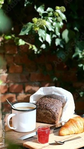 European hotel breakfast with croissant with marmelade, dark bread with bread knife and cup of coffee on wooden plank in hotel garden photo